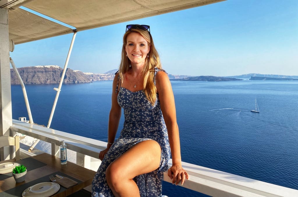 Santorini, Greece Travel Guide: Essential Tips for First-Time Visitors 6 Woman sitting on ledge in Santorini Greece at the Pelekanos Restaurant