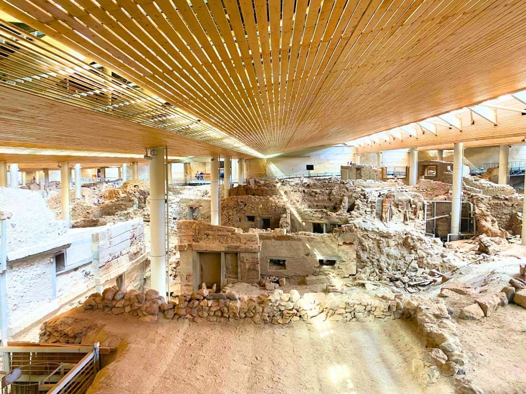 Santorini, Greece Travel Guide: Essential Tips for First-Time Visitors 10 Interior view of the Akrotiri archaeological site on Santorini, Greece, showing excavated ancient stone buildings and streets preserved under a modern protective roof with wooden beams and support columns above.