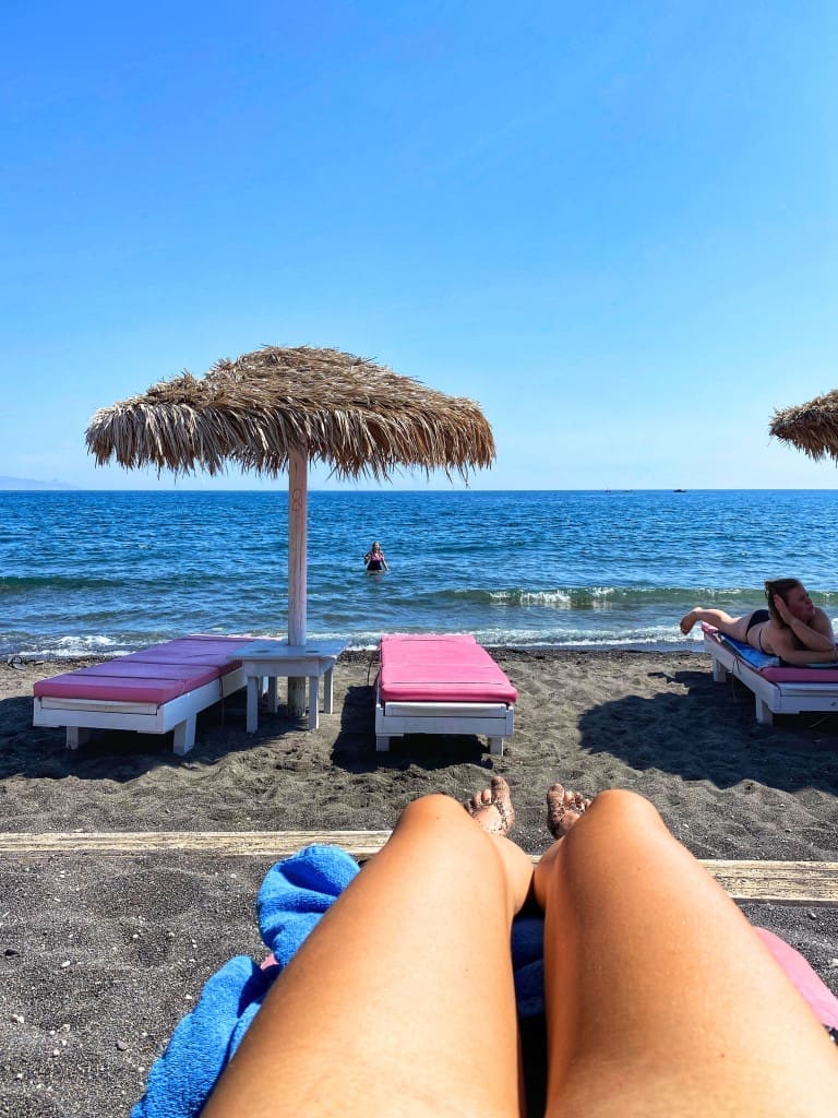 Santorini, Greece Travel Guide: Essential Tips for First-Time Visitors 12 Legs of a woman looking out at Perissa Black Beach in Santorini Greece